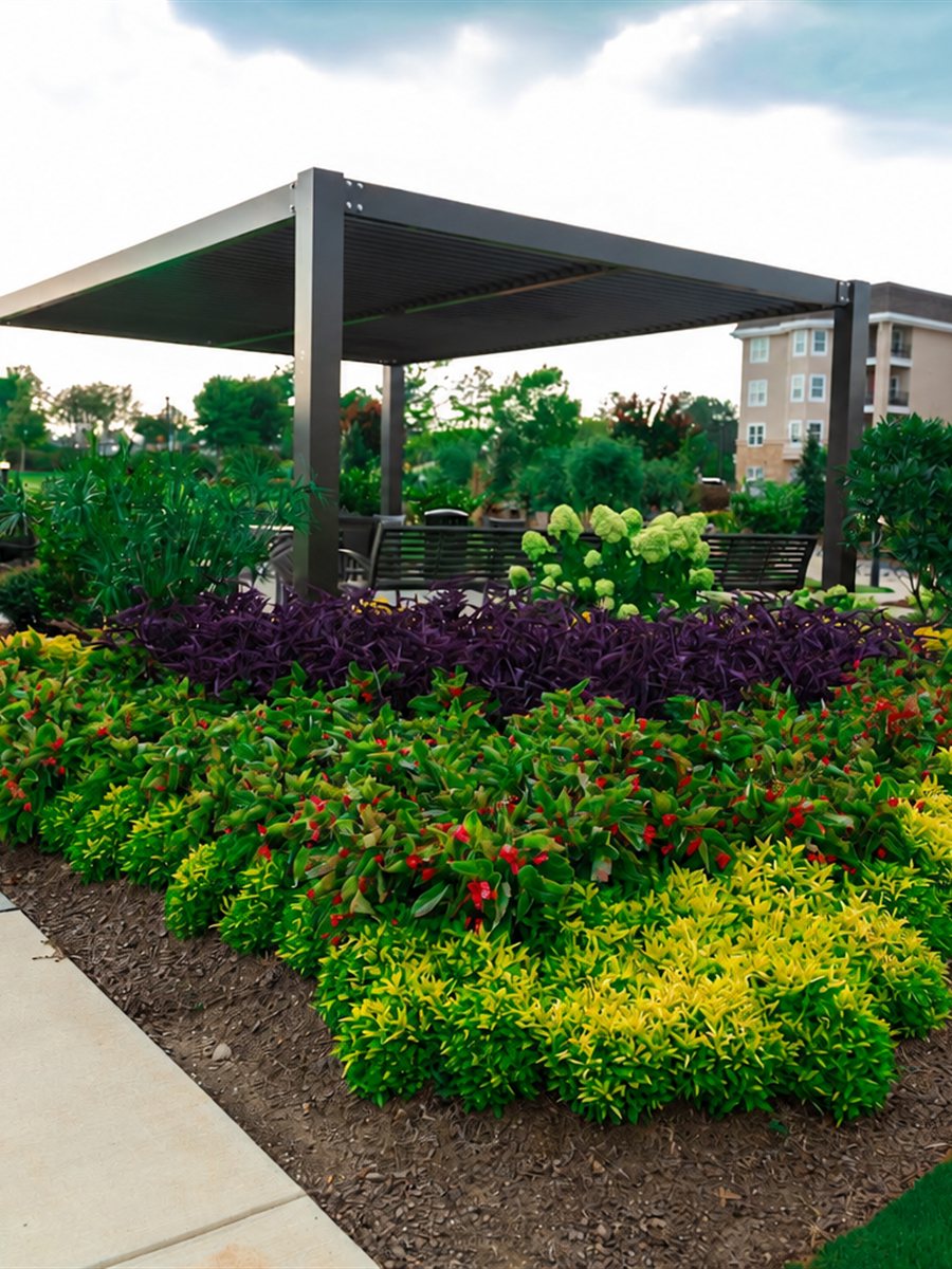 Layered seasonal color and shrub bed beside a shade pavilion at a community amenity