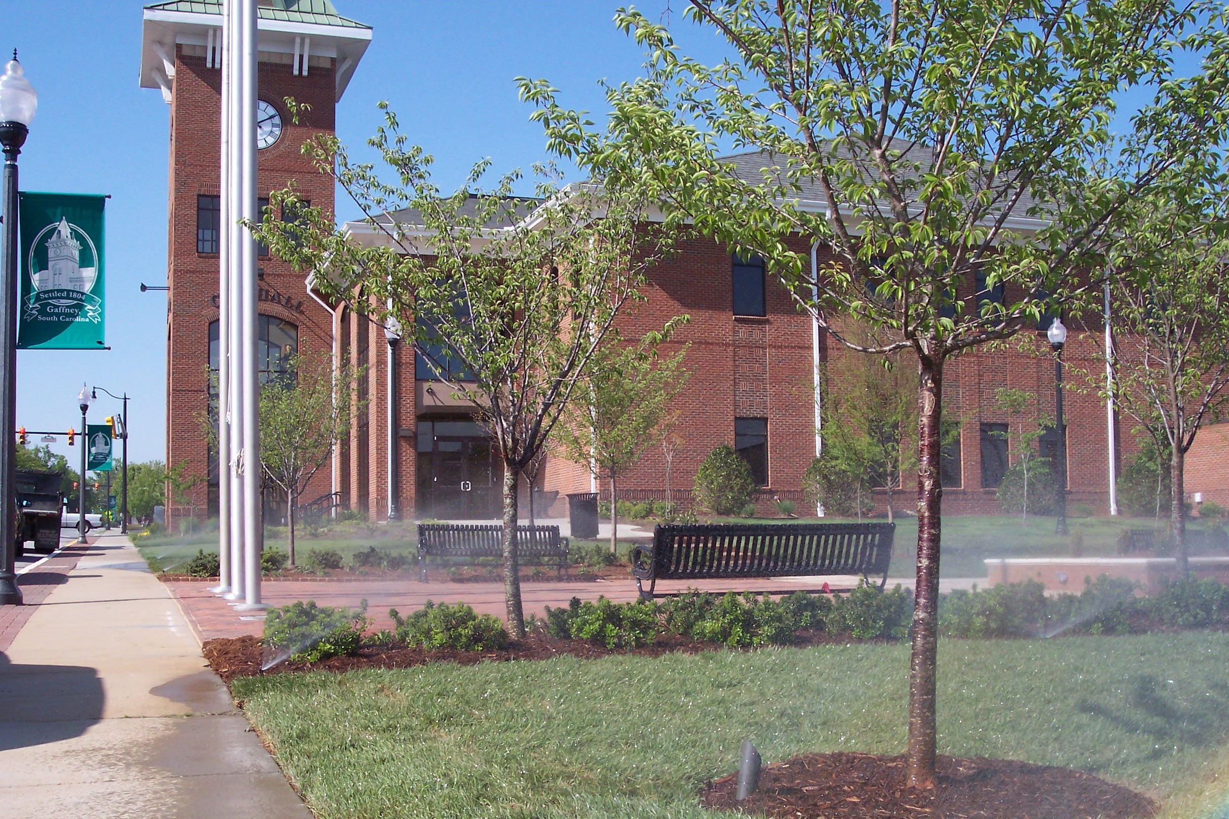 Irrigation heads watering newly planted trees and beds outside a municipal building
