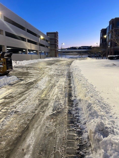 Plowed and treated drive lane beside a commercial parking garage at dawn